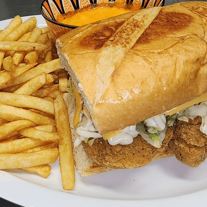 Crispy fried chicken sandwich with lettuce, sauce, and cheese, served with fries and a side of queso.
