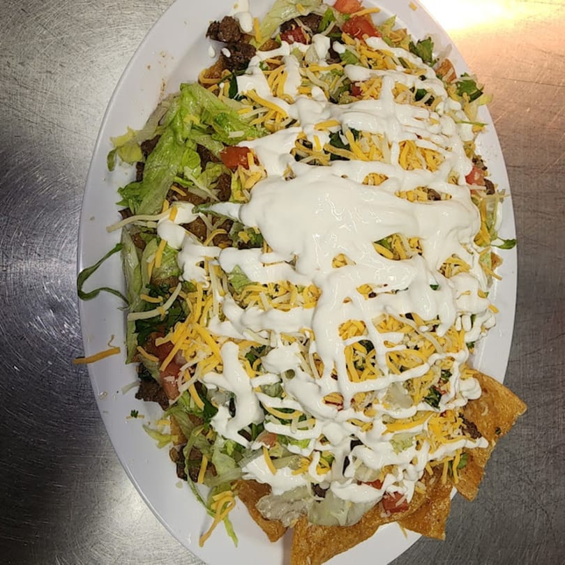 A large platter of Latin Bliss nachos with ground beef, lettuce, tomatoes, cheese, and sour cream.