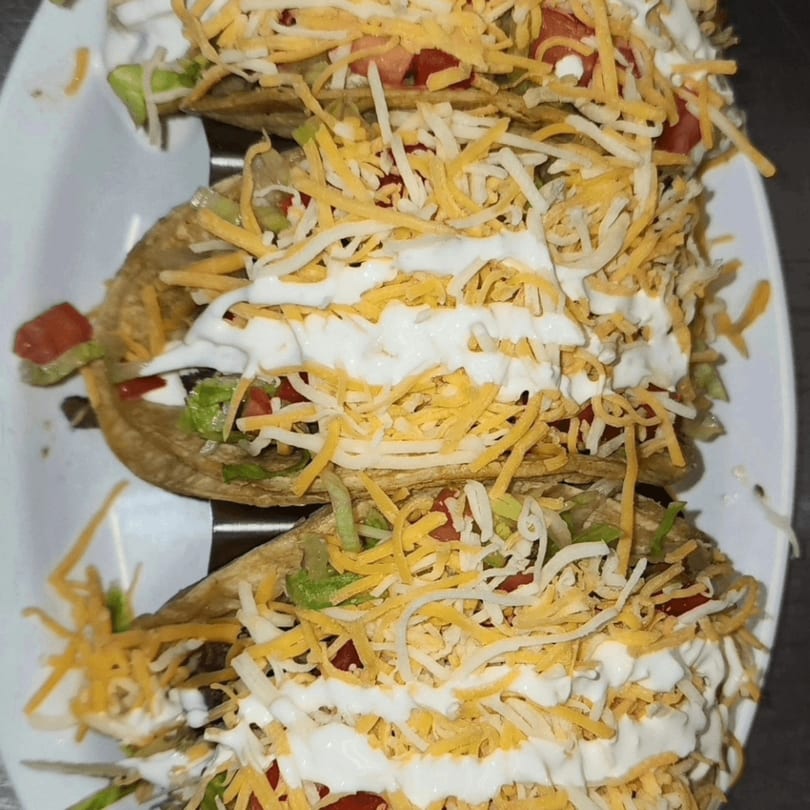 Three Latin Bliss tacos filled with meat, lettuce, tomatoes, cheese, and sour cream.