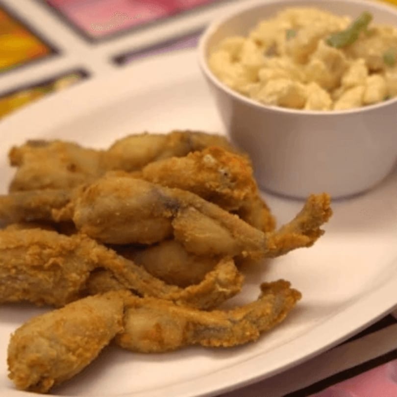 Fried frog legs on a white plate with a side of potato salad, from Latin Bliss.
